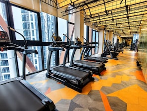 A gym with treadmills aligned along a wall with large windows, a patterned floor, and a ceiling with exposed beams. - Scarletz KLCC By Solvane Hospitality  (Kuala Lumpur)