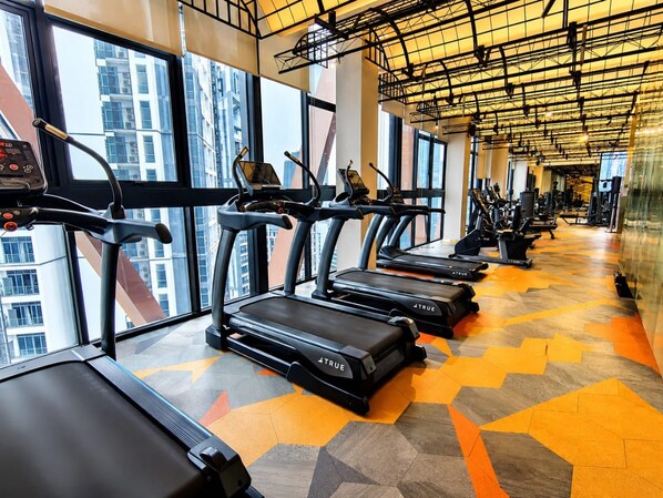 A gym with treadmills aligned along a wall with large windows, a patterned floor, and a ceiling with exposed beams. - Scarletz KLCC By Solvane Hospitality  (Kuala Lumpur)