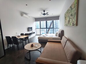 A modern living room with a sofa, a dining table with chairs, a TV, and a large window with a city view. - Scarletz KLCC By Solvane Hospitality  (Kuala Lumpur)