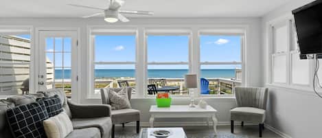 A living room with a view of the ocean, a ceiling fan, and a television mounted on the wall.