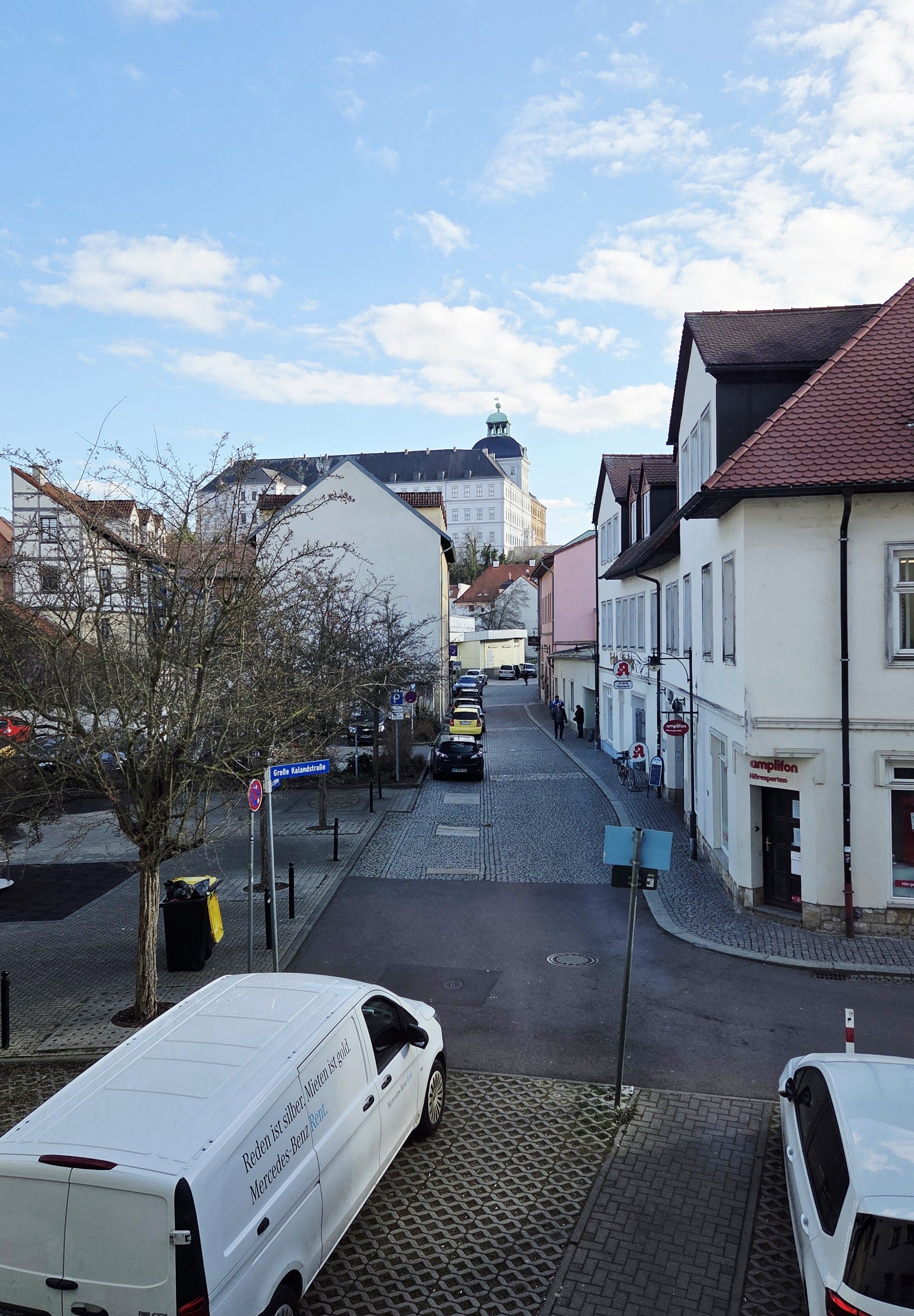 A cobblestone street lined with buildings, a white van parked on the side, and a clear sky.
