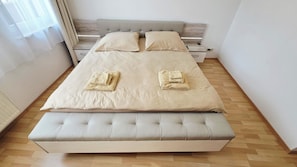 Ein ordentlich bezogenes Bett mit Kopfteil, einem Nachttisch und einer Sitzbank am Fußende.