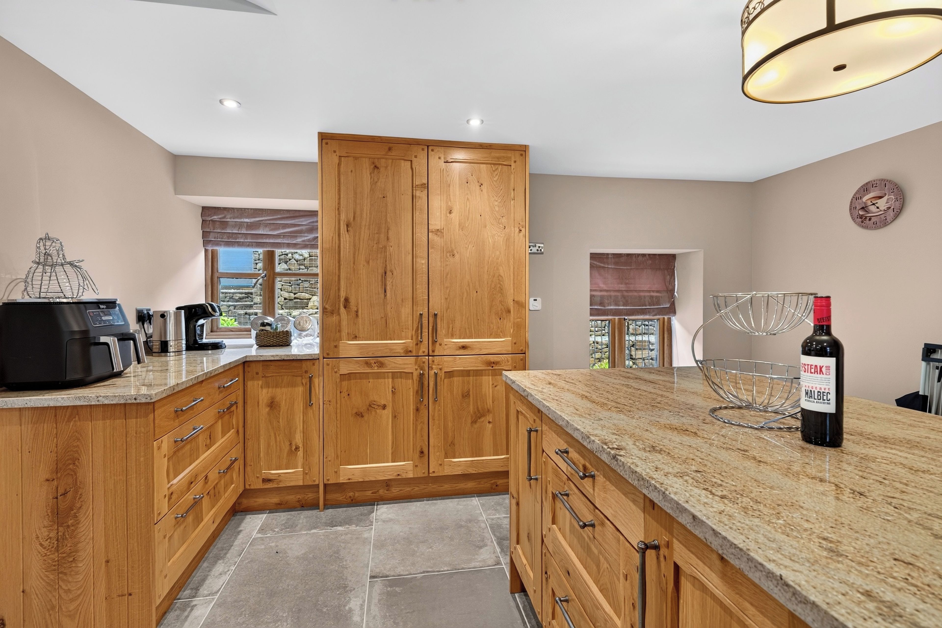 A kitchen with wooden cabinets, a granite countertop, a wine bottle, and a coffee machine.