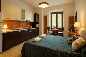 A compact hotel room with a kitchenette, a bed with rolled towels, a dining area, and a window with a view. - RELAX Palace (Roma)