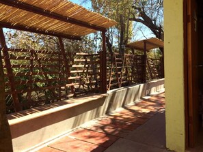 Una estructura de pérgola de madera con suelo de baldosas, rodeada por una valla de madera y árboles.