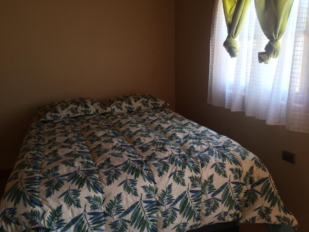 A bed with a leaf-patterned bedspread in a room with a window and curtains.