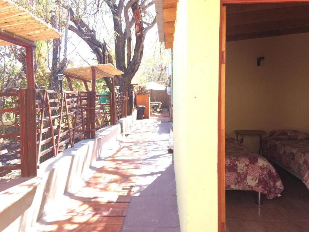 Una terraza de madera con sillas y mesas, un área techada y una habitación con cama y ventana.