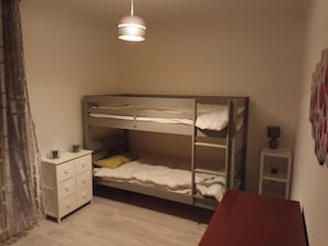 Habitación con literas, un aparador blanco, una mesita pequeña y una lámpara colgante.