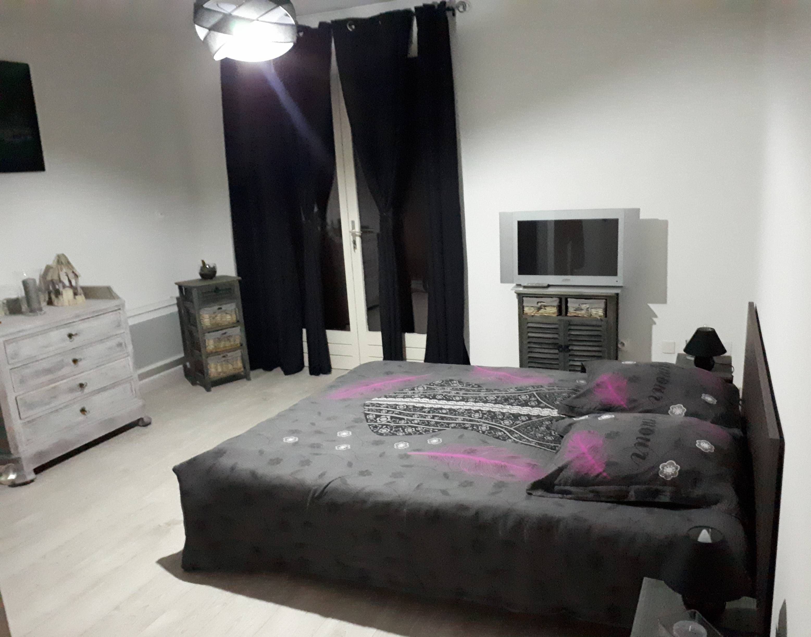 Quarto com cama, penteadeira, televisão e cortinas.