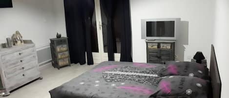 Quarto com cama, penteadeira, televisão e cortinas.