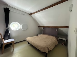 Ein Schlafzimmer mit einem Bett, einem Sessel, einem runden Spiegel und einem Fenster.