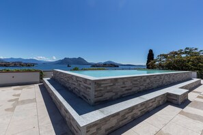 Une piscine bordée de pierres, entourée d’une terrasse carrelée, qui offre une vue sur un lac et, au loin, sur des montagnes.