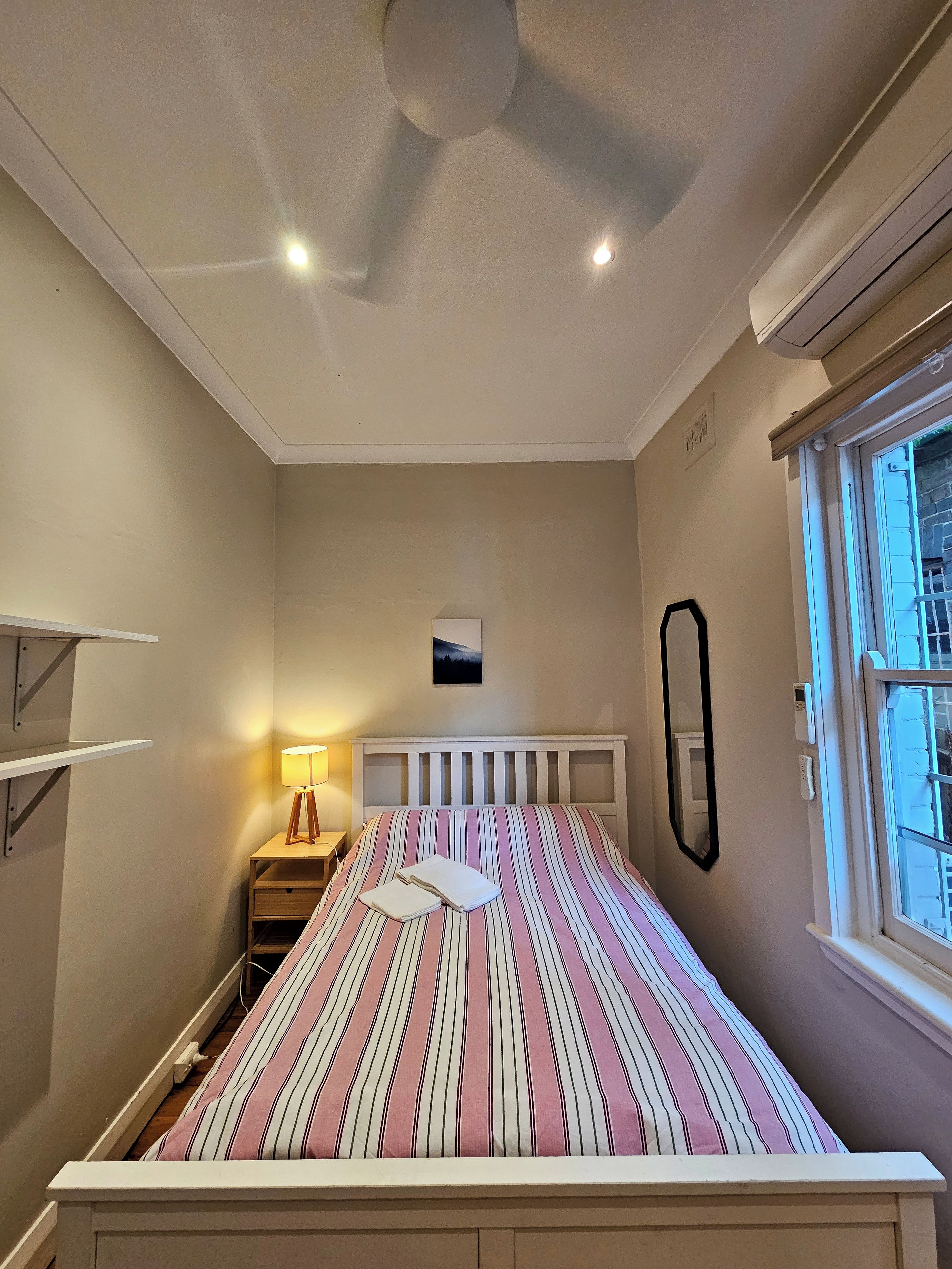 Une chambre à coucher avec un lit, une table de chevet, une lampe et une fenêtre.