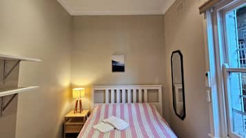 Une chambre à coucher avec un lit, une table de chevet, une lampe et une fenêtre.