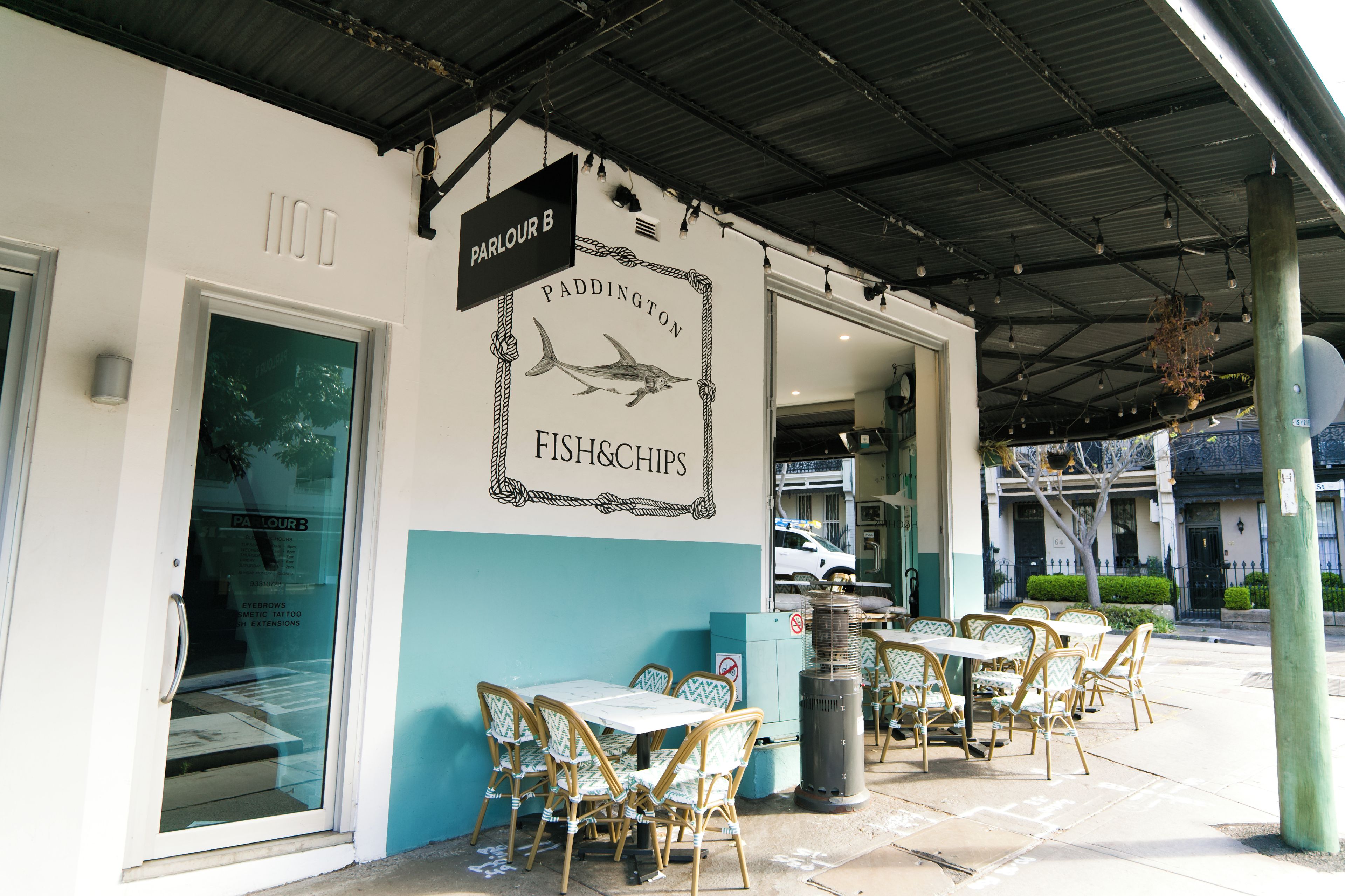 An outdoor seating area with tables and chairs, a sign for 'PADDINGTON FISH&CHIPS', and a covered walkway.