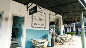 An outdoor seating area with tables and chairs, a sign for 'PADDINGTON FISH&CHIPS', and a covered walkway.