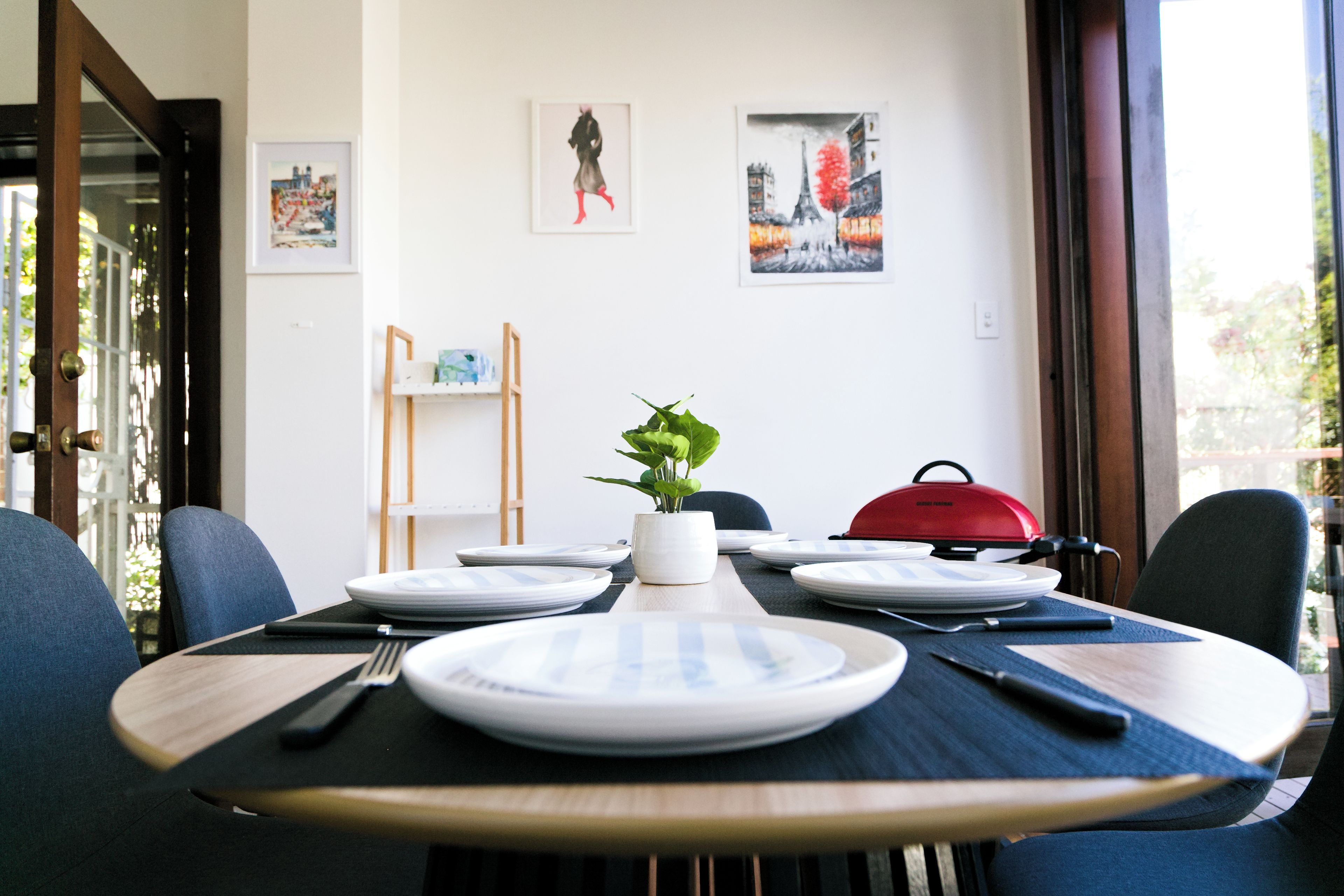 A dining area with a table set for two, a red grill, and artwork on the walls.
