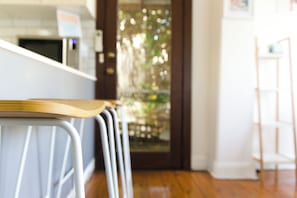 Una encimera de cocina con cubierta de madera y sillas de metal, un refrigerador y una puerta que da a un jardín.