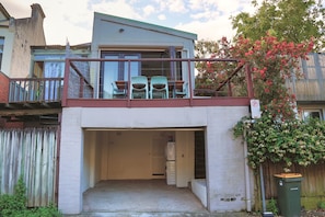 Un edificio residencial con balcón, entrada a garaje y contenedor de basura visible.