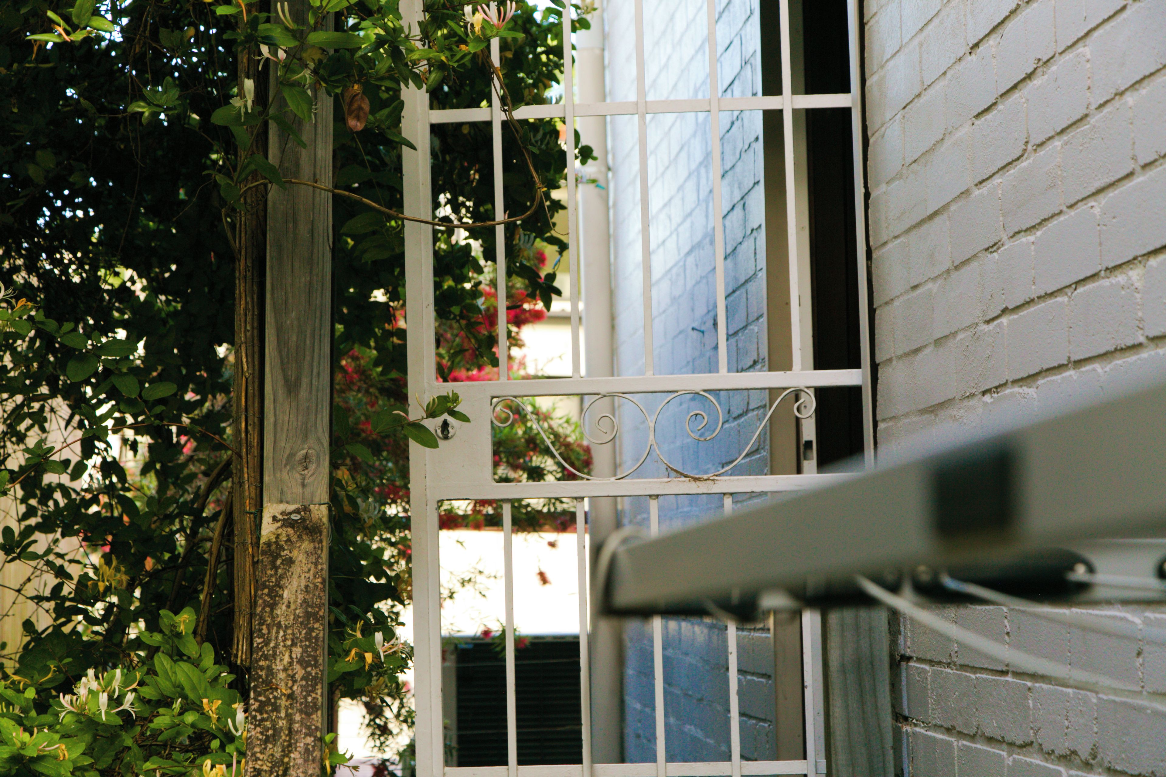 A white metal gate with a decorative top, a brick wall, and a window with blinds.