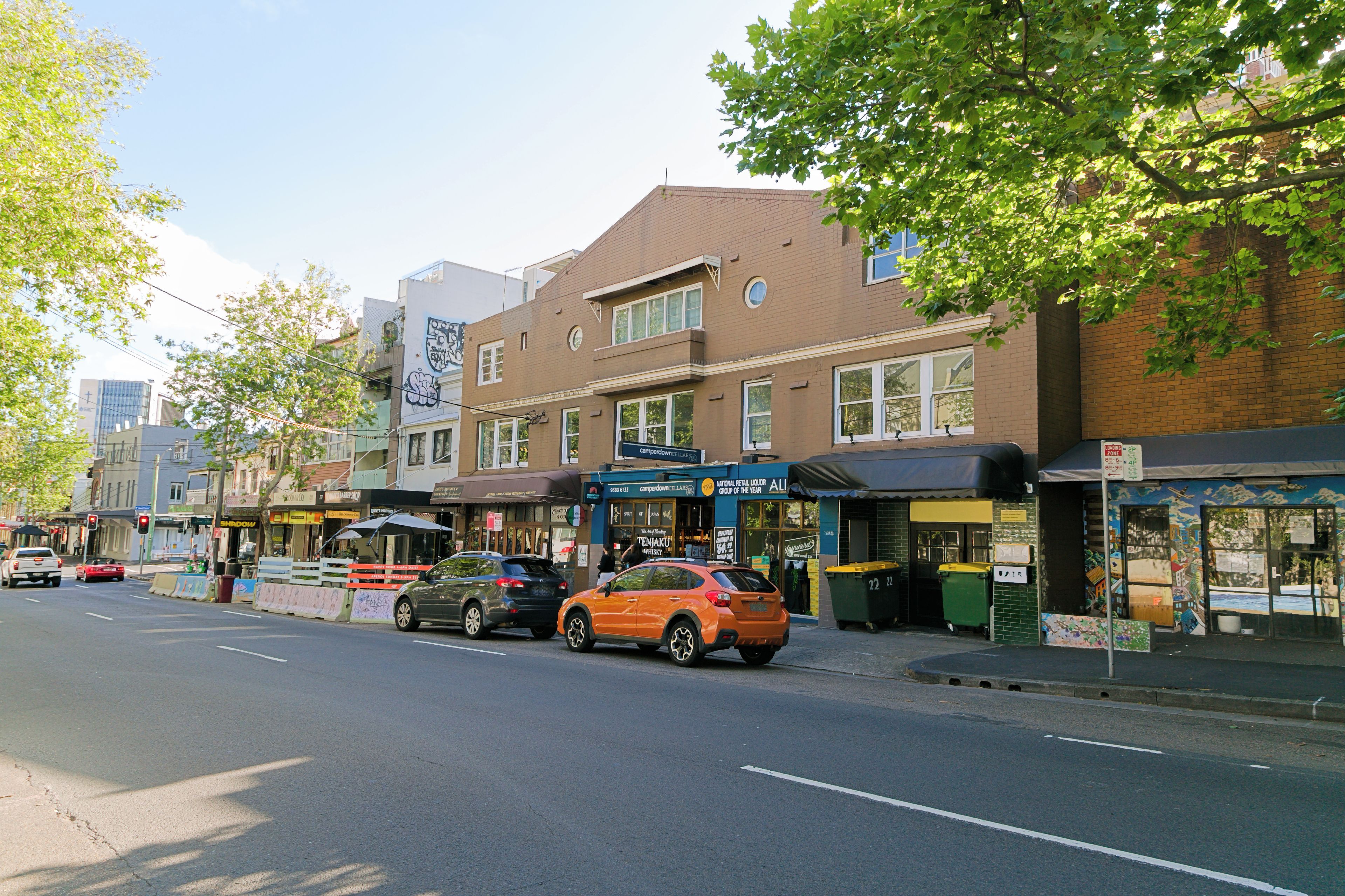 A street view with buildings, parked cars, and a clear sky.