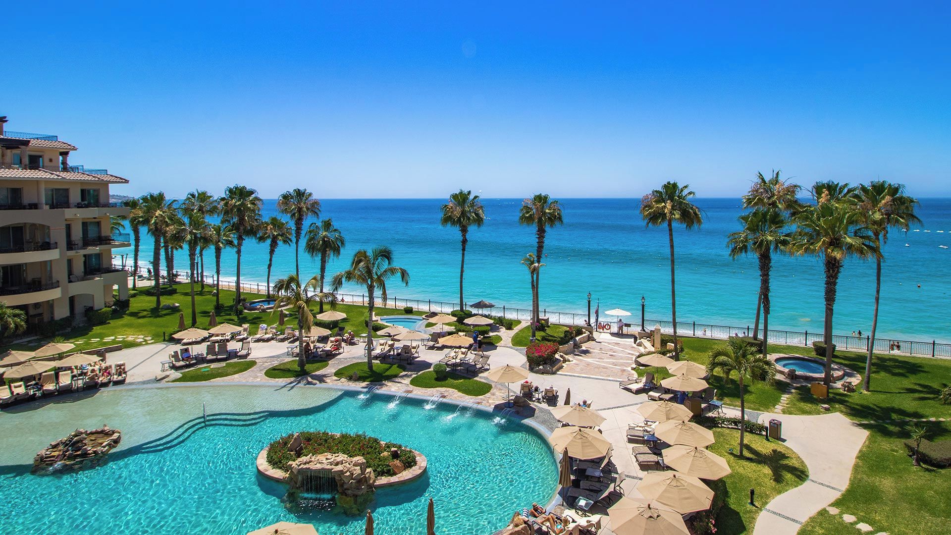Een resort met een zwembad, palmbomen en uitzicht op de oceaan.