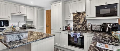 A modern kitchen with white cabinetry, a marble countertop, and stainless steel appliances.