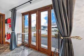 A room with a sliding glass door leading to an outdoor area, a small table, and fire extinguishers on the wall. - Pansy Lodge, this two-bedroom barn conversion sleeps 6. (Mydroilyn)