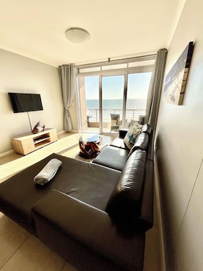 Habitación de hotel moderna con una cama grande, un televisor de pantalla plana, un mueble de madera y vista al mar.