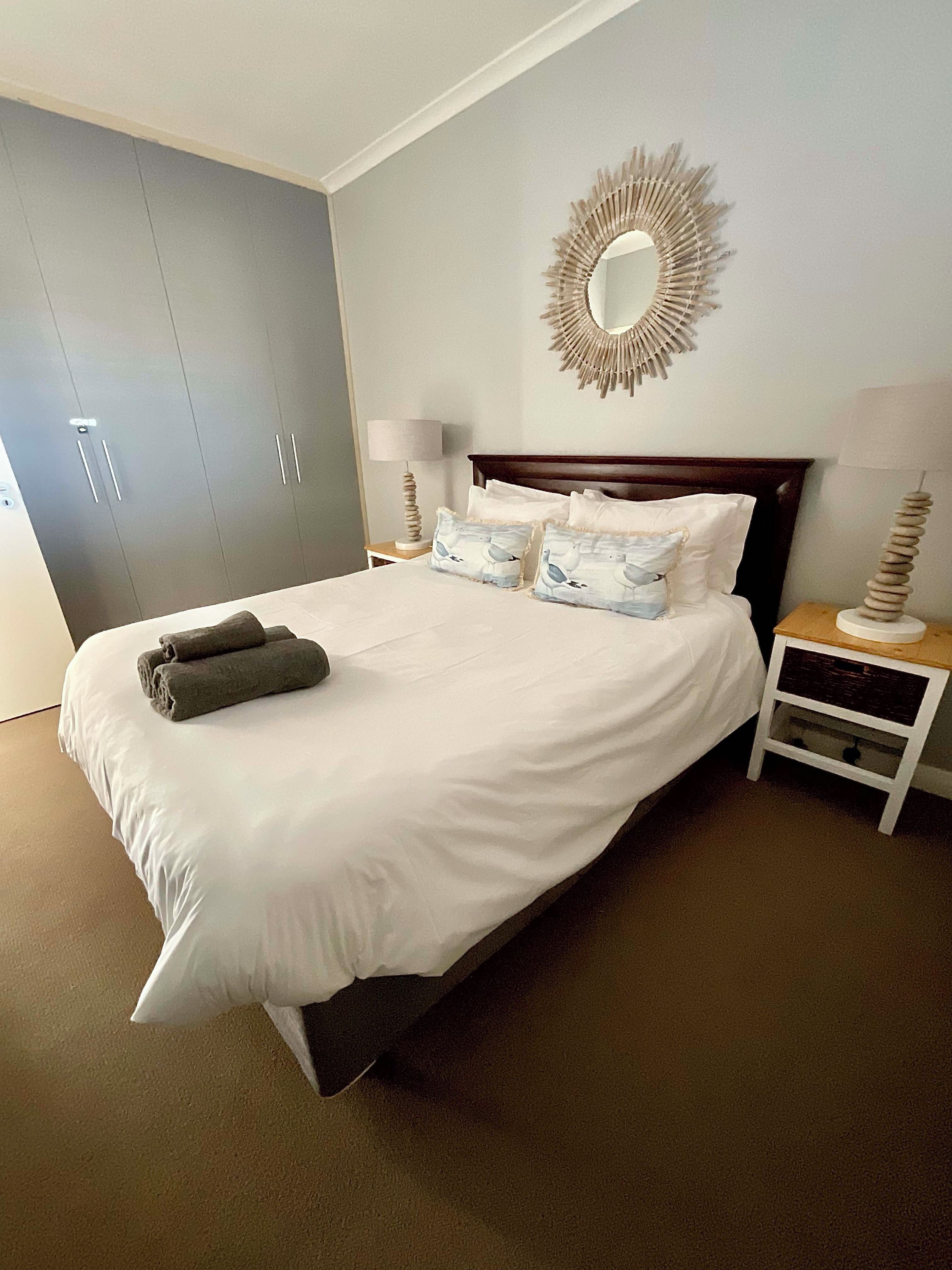 A hotel room with a large bed, a wardrobe, a bedside table with a lamp, and a wall-mounted mirror.