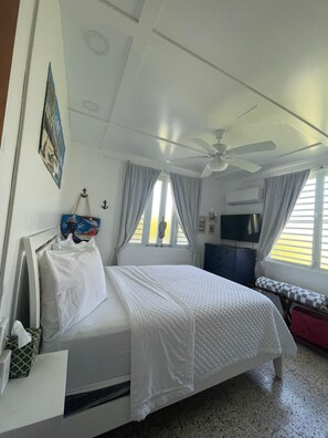 Ein Schlafzimmer mit Bett, Deckenventilator, Fernseher und einem Fenster mit Vorhängen.