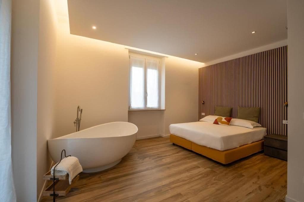 Un dormitorio moderno con una bañera grande, una cama con almohadas y una ventana con cortinas.