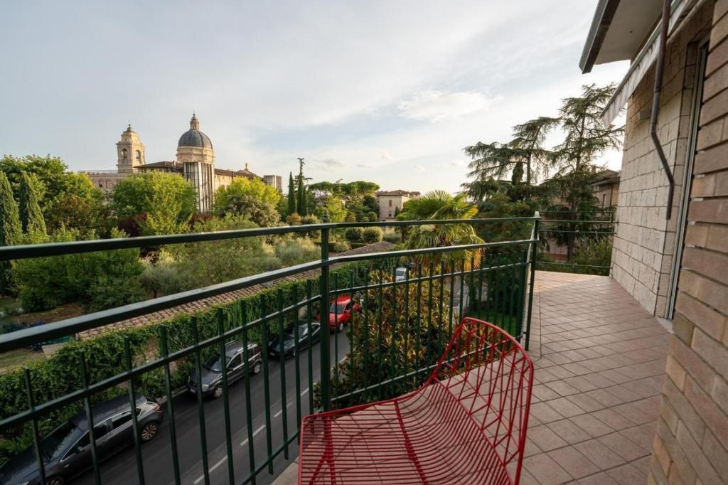 A balcony with a metal railing overlooking a street with parked cars and a building with a dome in the background.