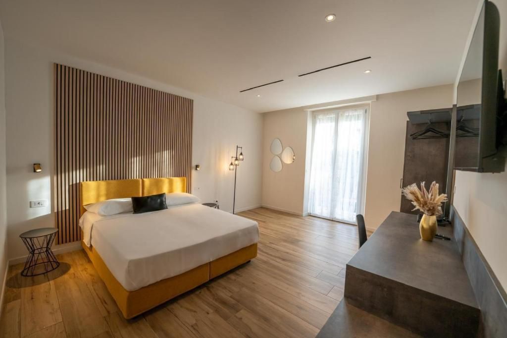 A modern bedroom with a large bed, a bedside table, a floor lamp, and a view of the outdoors.