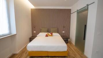 A modern hotel room with a large bed, a wooden floor, a sliding door, and a wall with vertical lines.