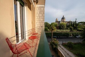Un balcón con sillas metálicas rojas y vistas a un edificio con cúpula.
