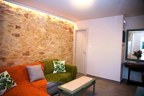 Un salon avec un mur en pierre, un canapé vert et une petite table.