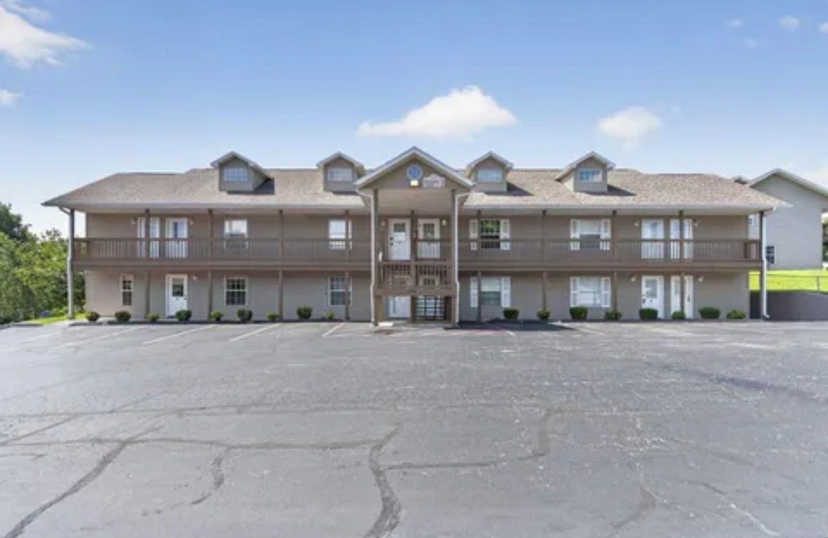 A multi-story motel with a central entrance, parking lot, and a clear sky.