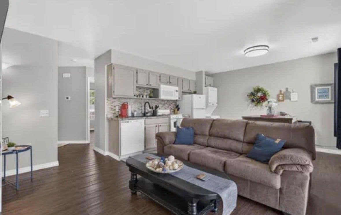 A modern living room with a sofa, a coffee table, and a kitchen in the background.