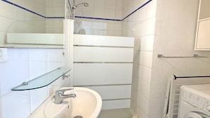 Un bany amb plat de dutxa de vidre, un lavabo i una rentadora.