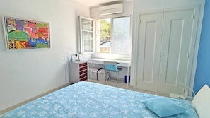 A bedroom with a bed, a desk, a chair, a window, and a door. - New Listing (Sainte-Maxime)