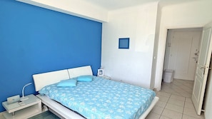 Un dormitori amb llit, taula de nit i porta que dona a una altra habitació.