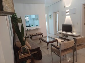 A modern living room with a glass coffee table, a sofa, a TV on a stand, and a large plant. - New Listing (Porto Alegre)