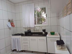 A compact kitchen with white cabinets, a gas stove, a coffee maker, and a window with a view of greenery. - New Listing (Porto Alegre)