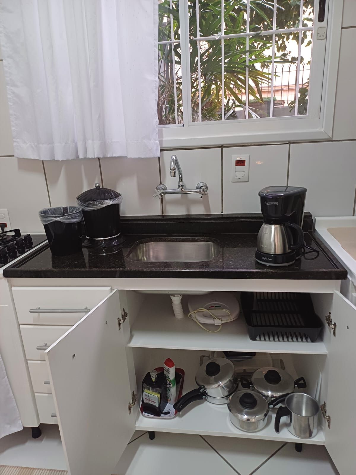 Uma cozinha com pia de aço inoxidável, cafeteira e diversos utensílios de cozinha.