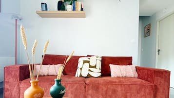 Un salon avec un canapé rouge, deux tables basses en bois et des vases décoratifs contenant des tiges de blé.