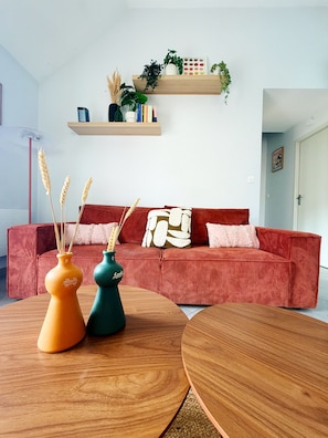Ein Wohnzimmer mit einem roten Sofa, zwei Holztischen und dekorativen Vasen mit Weidenähren.