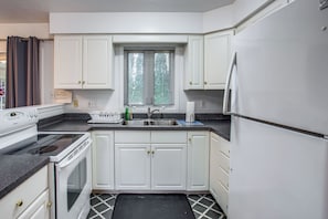 A kitchen with white cabinets, a black countertop, a built-in stove, a sink, and a window with blinds. - Hot Tub Haven with Game Room Home with In-Law Suite (Rochester)