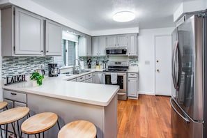 Eine moderne Küche mit weißen Schränken, einem Edelstahl-Kühlschrank, einem Einbauofen und einer Kaffeemaschine.
