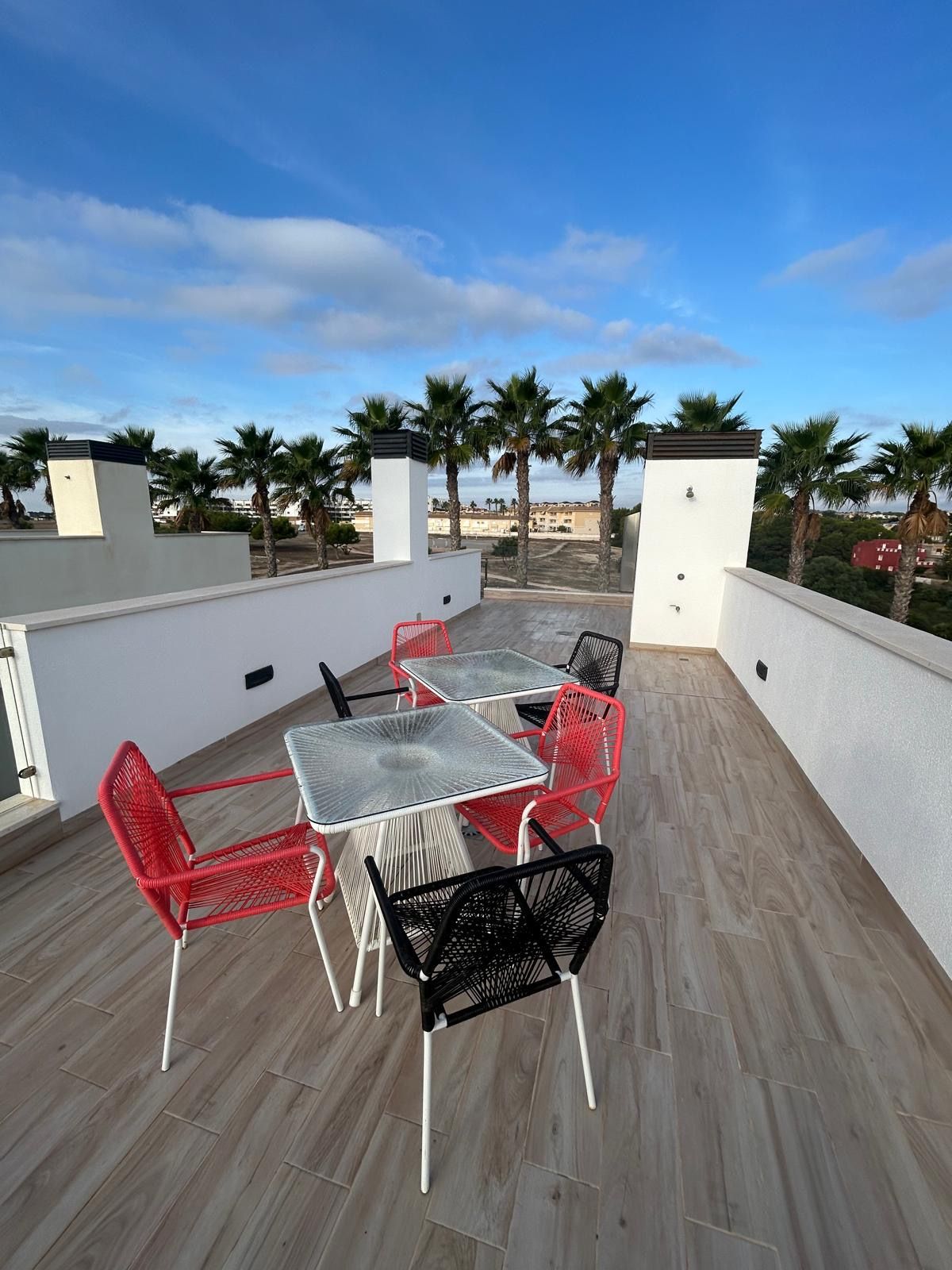 Eine Terrassengruppe mit Tisch und Stühlen, umgeben von Palmen und wolkenlosem Himmel.